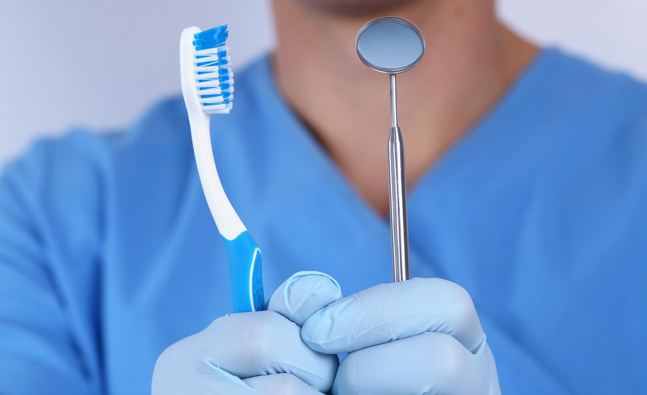 Der Zahnarzt hält eine Zahnbürste und einen zahnärztlichen Spiegel in der Hand, welche wichtige Mittel in der Vorbeugung der Zahnfleischentzündung sind.